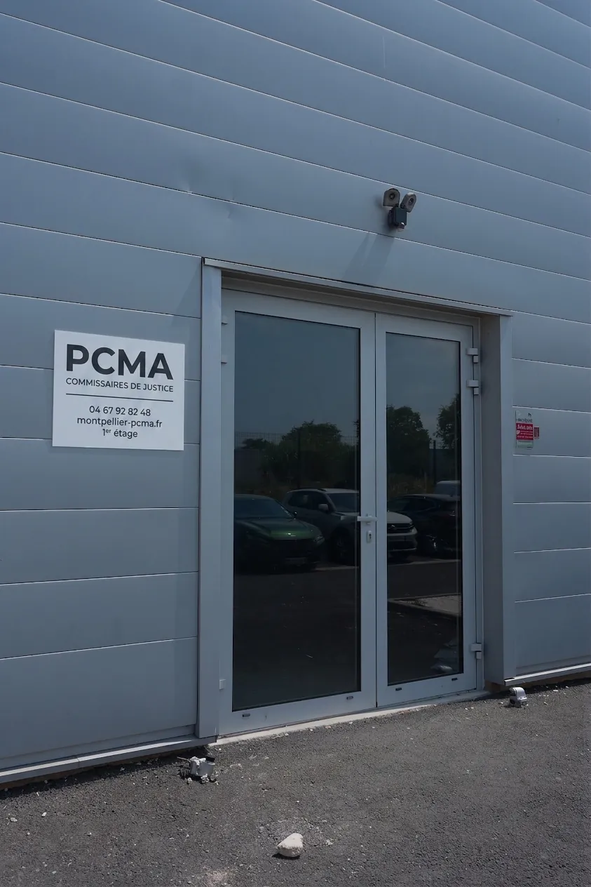 Entrée de l'étude PCMA : porte vitrée sur façade grise, plaque PCMA Commissaires de justice à gauche